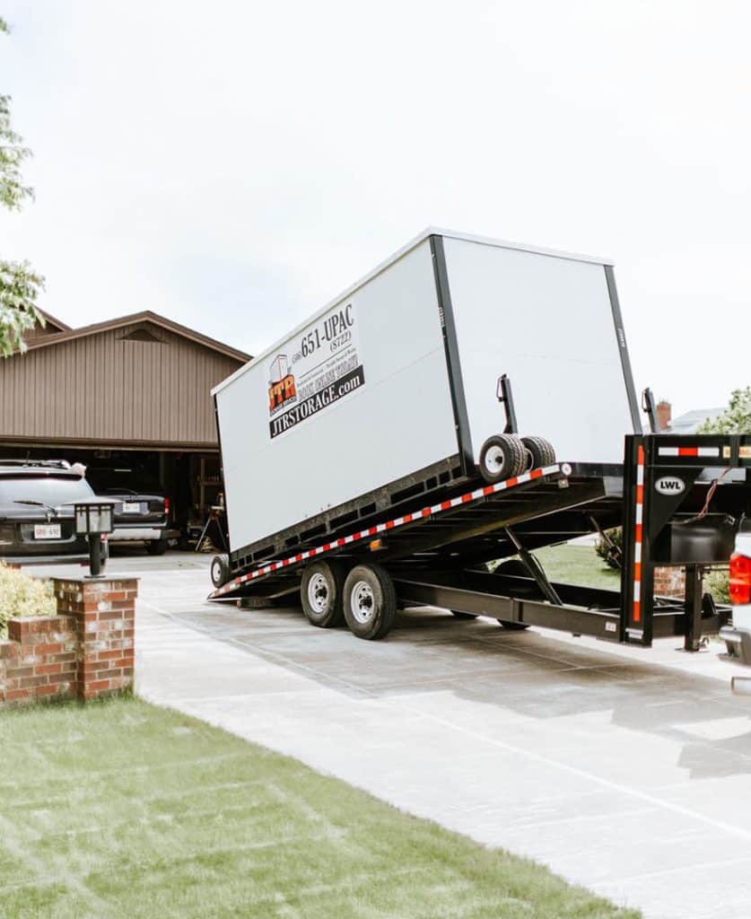 A Boxwell mobile storage bin being unloaded at a residence with a tilt-back trailer.