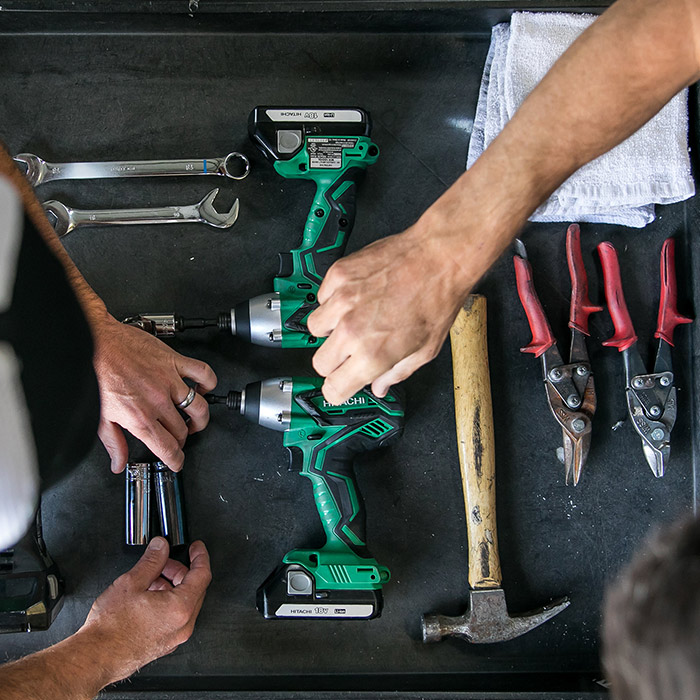 Close-up of two workers arranging green Hitachi power drills, wrenches, pliers, and a hammer on a workbench, representing Boxwell’s commitment to quality craftsmanship and reliable warranty services for its portable storage units
